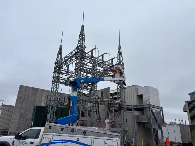 A Hydro bucket truck is in front of an electrical structure. A powerline technician is in the raised bucket.