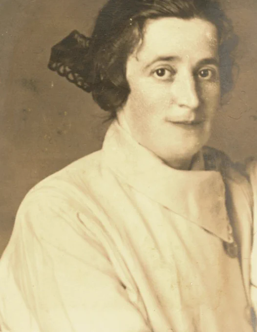 Vintage portrait of a woman wearing an elegant outfit with her hair styled up, looking directly at the viewer.
