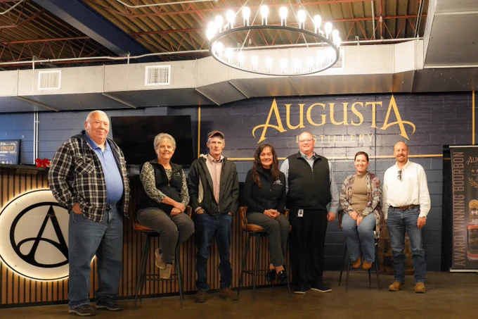 CED team and Augusta team posing in front of Augusta Distillery sign inside the distillery