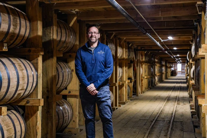 Augusta team member standing in their rickhouse, smiling with barrels of bourbon aligning the walls