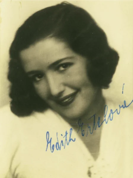 Vintage portrait of a woman smiling, with her signature in blue ink at the bottom right of the image.
