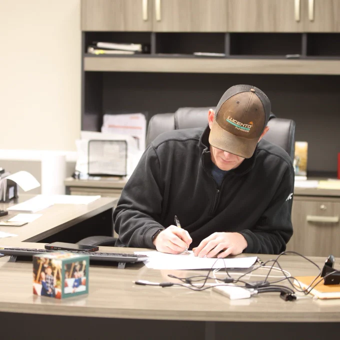Farmer sitting at desk signing a piece of paper. 