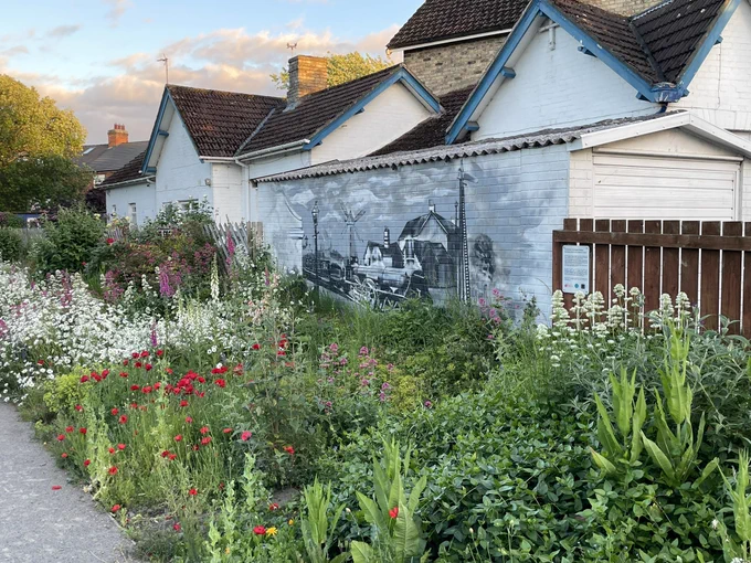 A wide flower border in front of a black and white mural of a train on the old railway station