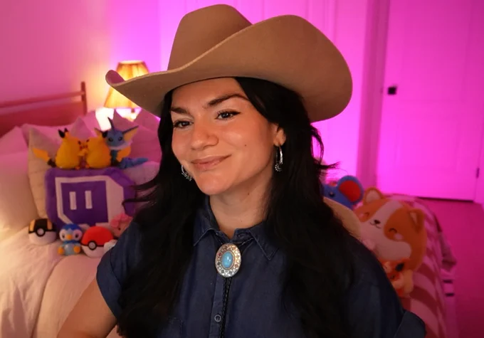 dark haired girl in denim shirt with bolero tie and cowboy hat. On pink backdrop