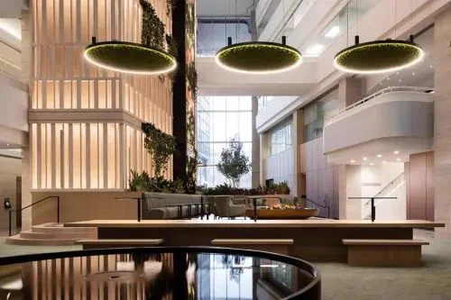 Bright modern atrium with large circular green light fixtures, vertical garden wall, cozy seating, and floor-to-ceiling windows, conveying an airy, natural feel.