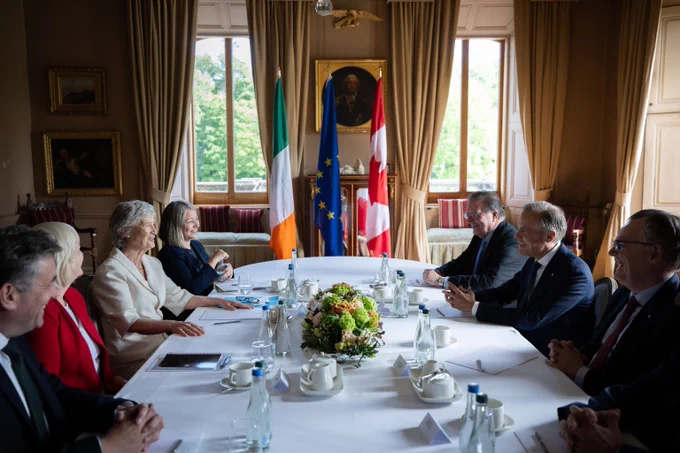 Le premier ministre Carney rencontre la présidente de l’Irlande, Catherine Connolly, durant sa visite bilatérale en Irlande. Ils sont assis face à face, en présence de hauts responsables, et les drapeaux du Canada, de l’Union européenne et de l’Irlande sont disposés dans la salle.