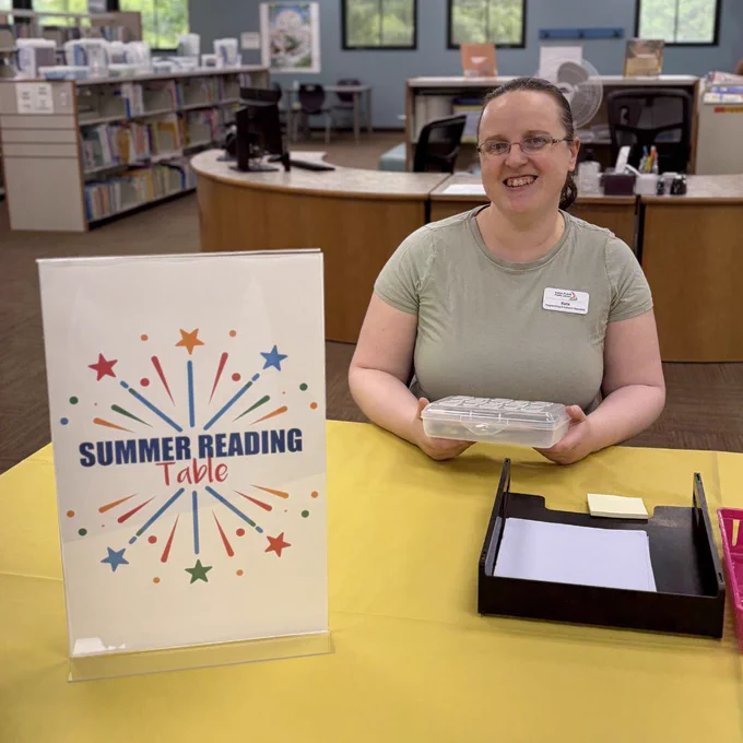 Staff member sitting at Summer Reading Table.