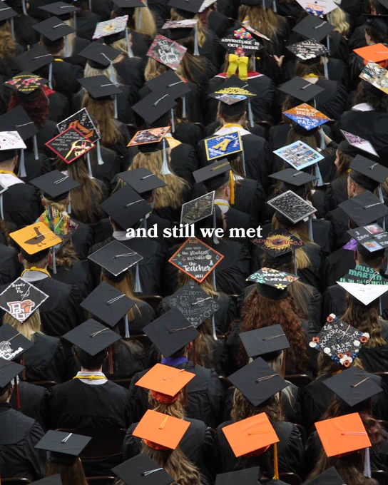 A large gathering of graduates in caps and gowns is viewed from above. Their caps are creatively decorated with various designs and phrases. In the center of the image, the words "and still we met" are visible.