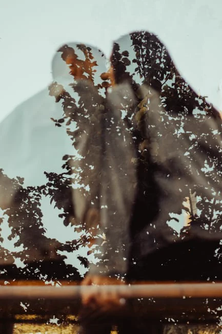 A romantic silhouette of a couple embracing, visible through a window with tree reflections.