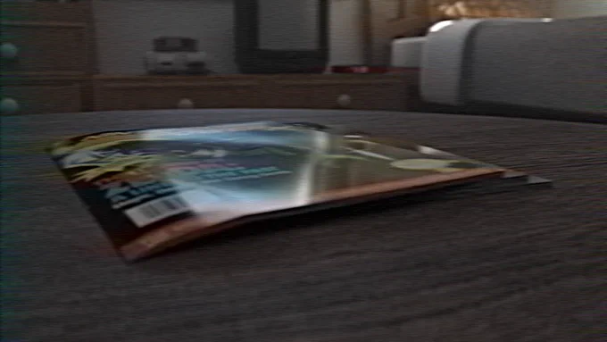 A slightly distorted, low-angle shot of a glossy magazine lying flat on a dark wooden surface. The background is a softly blurred bedroom setting with a dresser and bed. The entire image has a subtle VHS-style scanline and glitch effect.