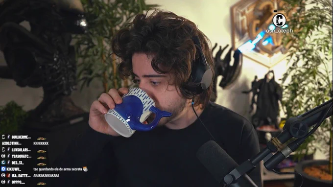 Screenshot of Cellbit's stream screen. He's wearing a black sweater and holding a whale-themed mug. The Twitch chat is on the bottom left corner.