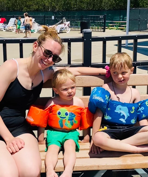 A mom and her two young boys wearing floaties sitting on a bench by the kiddie pool at the Parma Heights Community Pool opening