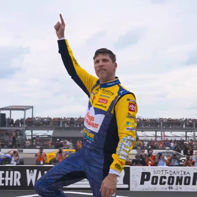 Denny Hamlin in a blue and yellow minion suit pointing at the sky.