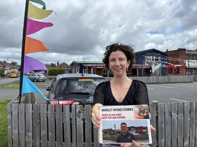 Anneliese stood holding a leaflet with Andy Burnham on it with a pub in the background, stood in the same pose for her photo as Andy was in his leaflet ie with the same pub behind.