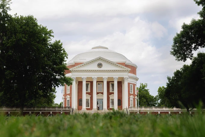 The Rotunda at the University of Virginia surrounded by green trees under a partly cloudy sky.