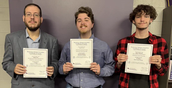 Three individuals standing and smiling while holding certificates from the Society of Collegiate Journalists. They are positioned in front of a gray wall.
