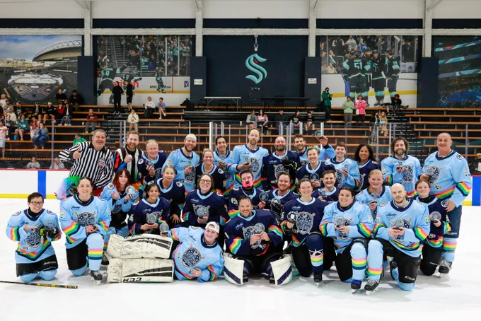 a group photo of a hockey team in light and navy blue posing for a photo on the ice at Kraken Community Iceplex.