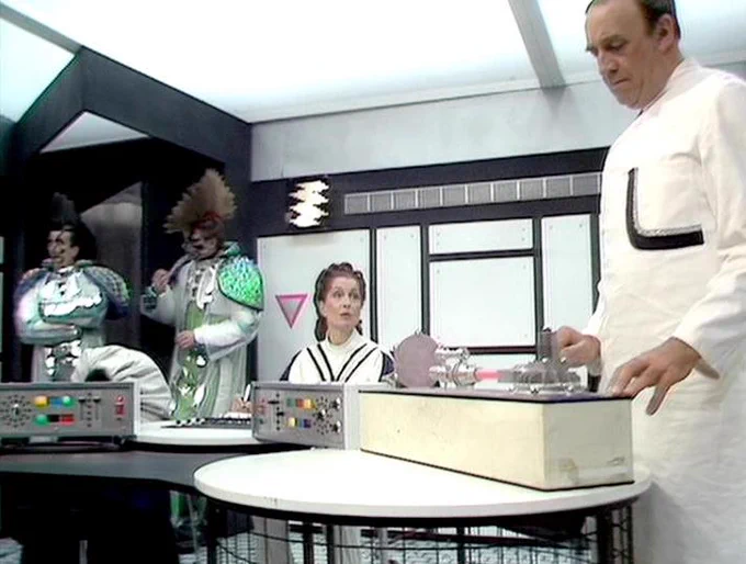 GPT 5.4 Nano describes the image as: "The image shows a tense moment aboard a futuristic spacecraft set in a bright, utilitarian interior with black-and-white panels, windows, and control consoles. Several performers in period-like, sci‑fi costumes cluster around electronics and monitors. Leonard Kavanagh appears in the foreground on the right, leaning over a large crate-like device on a wheeled table, gesturing as if preparing or operating equipment. In the background, others watch closely, including one seated behind a console and another in an ornate, clownish android-like costume. The overall scene suggests a technical operation or confrontation requiring precise control and teamwork."
The script search url for this tweet is
https://blake.torpidity.net/s/404/236