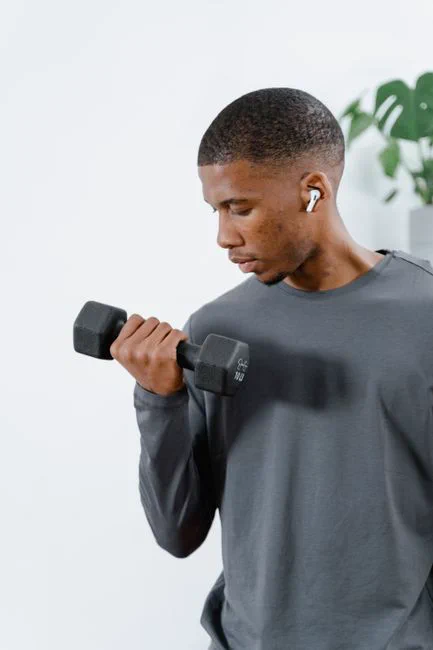 A young man in activewear lifting a dumbbell indoors, focused on fitness.