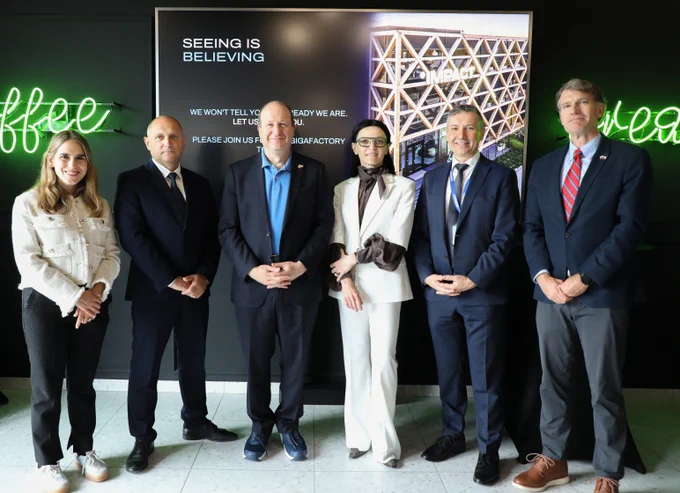 Six professionals in business attire stand in front of a digital display with the phrase 'Seeing is Believing' and a geometric design.