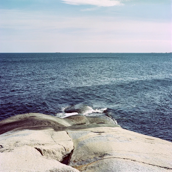 Rock formations going into the sea. Lightly cloudy sky over the horizon. Several small islands far away.