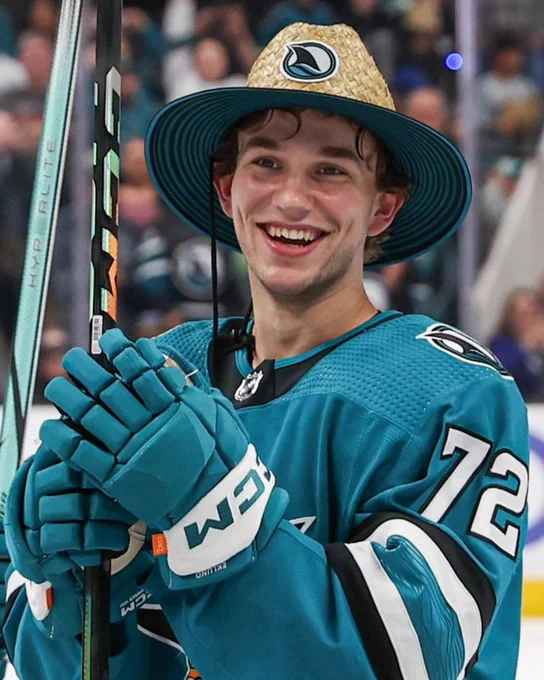 William Eklund on the ice in his teal Sharks jersey while wearing a straw hat 