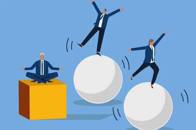 Businessman meditating calmly on a yellow cube while two colleagues struggle to balance on large white spheres against a blue background.