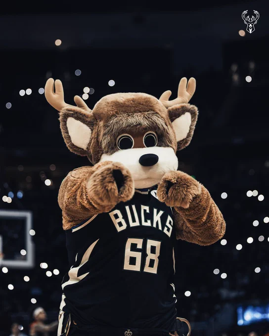 A photo of Bango pointing to the camera in a black Bucks jersey on the court at Fiserv Forum.