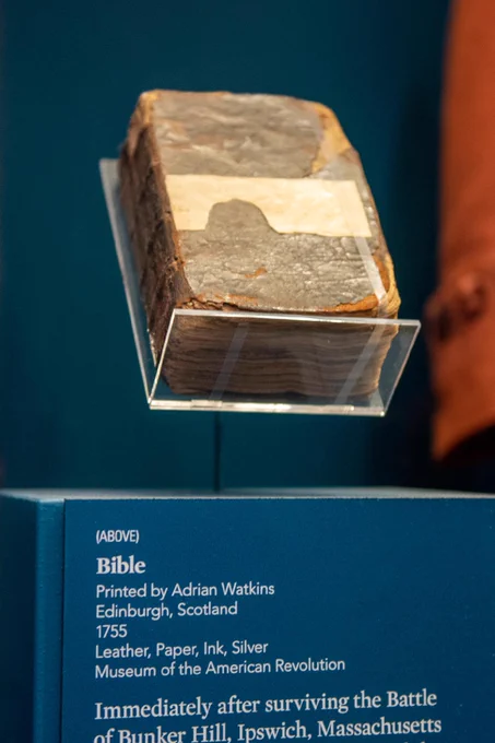 An old Bible exhibited on a clear stand. The label indicates it was printed by Adrian Watkins in Edinburgh, Scotland, in 1755. Displayed at the Museum of the American Revolution, it mentions the Bible’s connection to the Battle of Bunker Hill, Ipswich, Massachusetts.