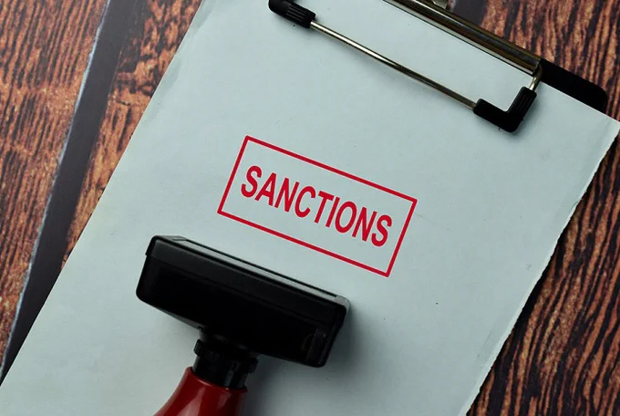 Close-up of a clipboard with a paper stamped in red ink reading 'SANCTIONS' on a wooden surface.
